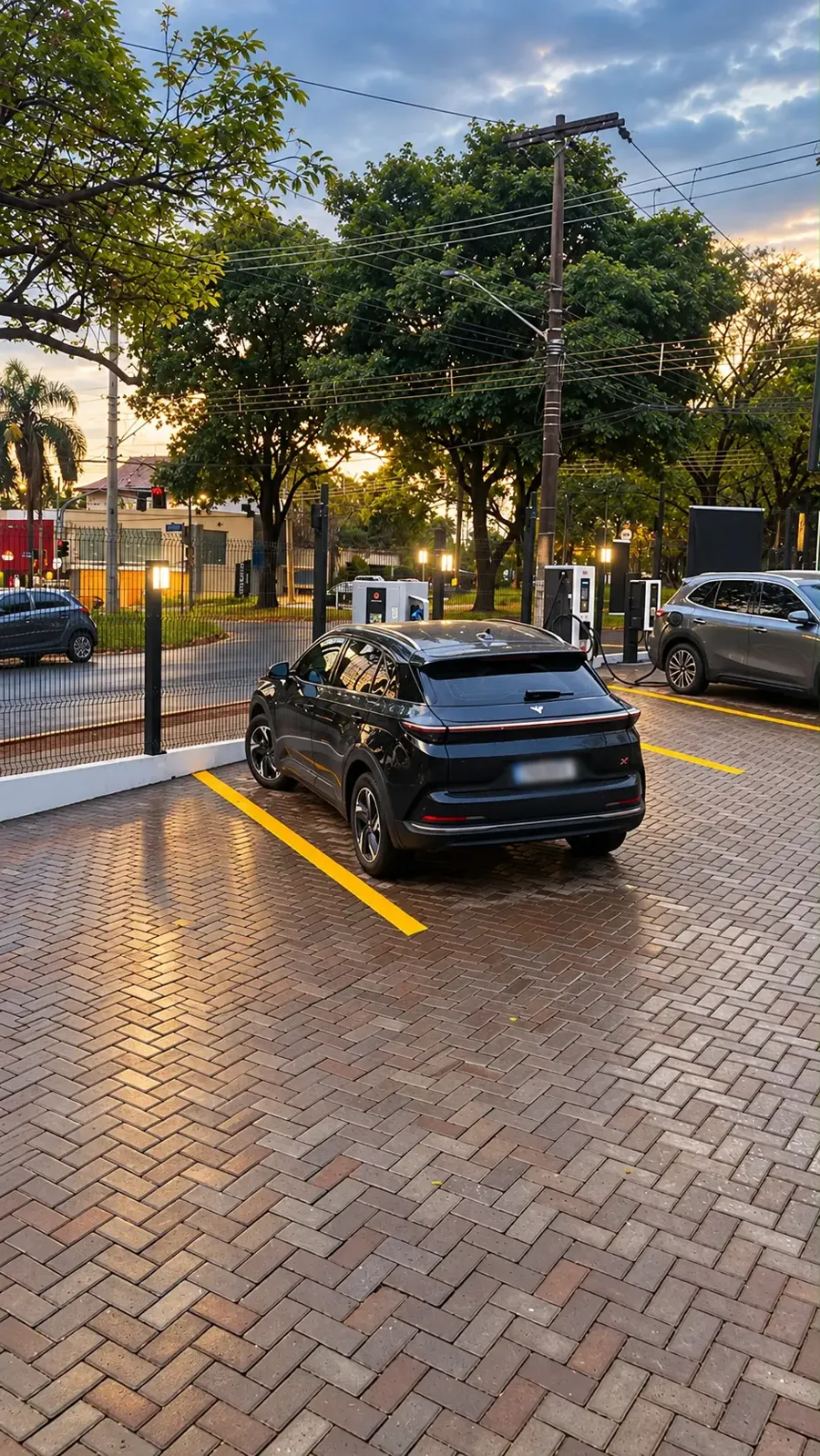 Carro elétrico preto estacionado na vaga demarcada com carregadores ao fundo